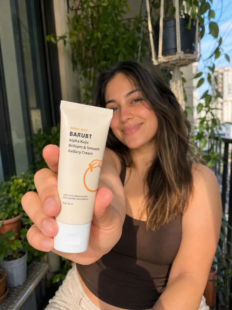 Young woman on a sunny balcony holding a tube of undim brightening cream