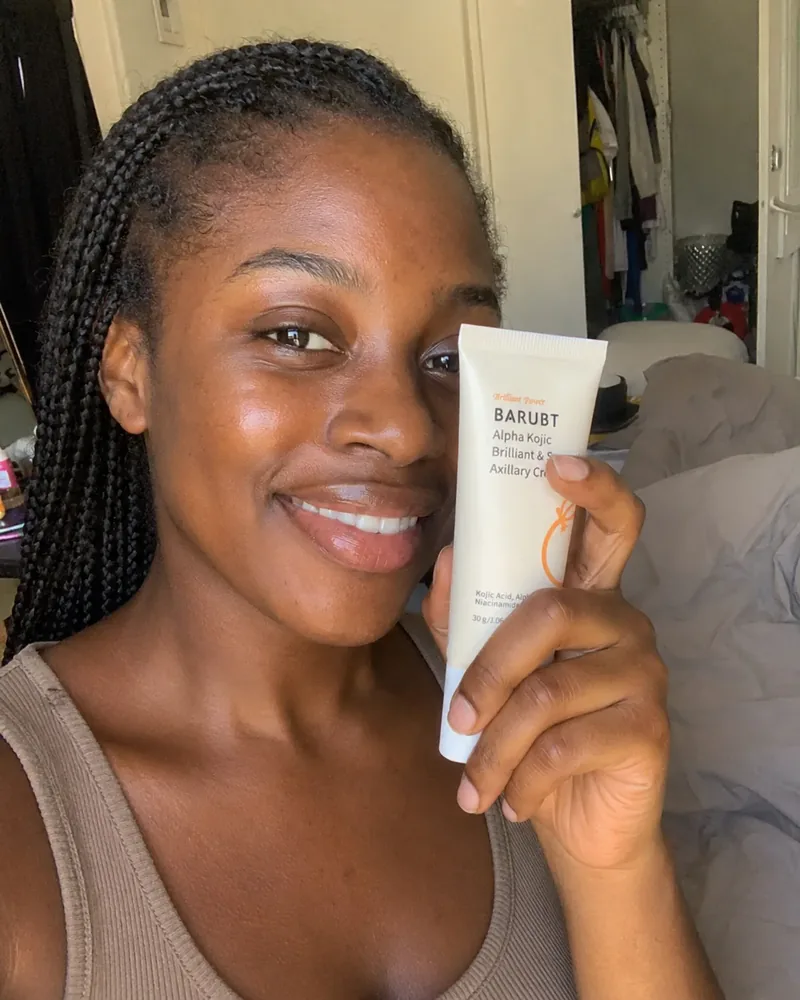 Smiling young woman holding a tube of undim brightening cream in her bathroom